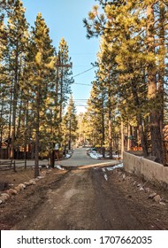 View of empty dirt road and pine trees surrounded by rustic cabins in the mountains after snow in California during winter sunset 