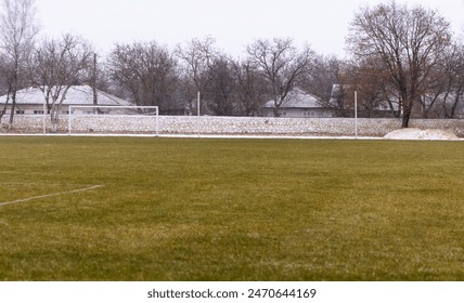A view of an empty football field covered in grass with gates and stands for spectators, in winter during cold season - Powered by Shutterstock