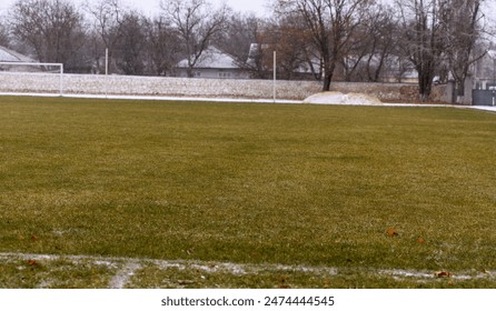 A view of an empty football field covered in grass with gates and stands for spectators, in winter sport during cold season - Powered by Shutterstock