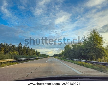 View of an empty highway surrounded by green trees under a cloudy sky, perspective of a driver on the A29 motorway near 262197 Alhorn, Germany