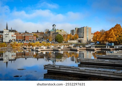 View from the empty marina harbour showing Brockville's city hall and downtown buildings with trees in autumn color, under a blue sky with a few clouds - Powered by Shutterstock