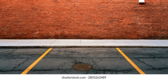 A view of an empty parking lot with yellow lines marking spaces, leading up to a textured red brick wall with a white stripe.