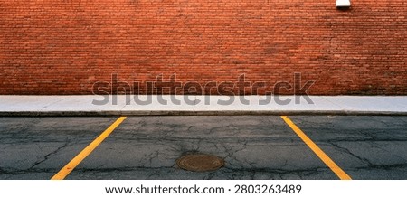 A view of an empty parking lot with yellow lines marking spaces, leading up to a textured red brick wall with a white stripe.