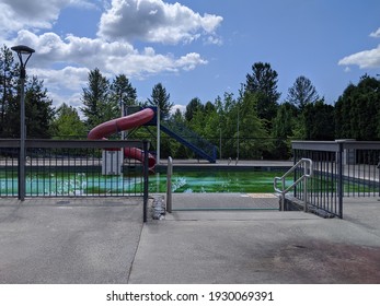 View Of An Empty Public Pool With A Large, Red Waterslide On A Bright, Sunny Day