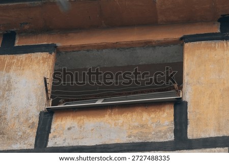 A view of an empty window opening in a destroyed residential building. The missing frame and surviving clotheslines highlight the extent of the damage to the façade following a direct hit or powerful explosion.