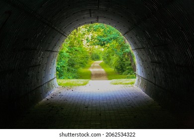 View Of End Of Dark And Empty Tunnel Under The Bridge In A Forest In Summer With Hiking Trail And Trees In Background. No People.