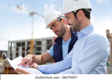 View Of A Engineer And Worker Watching Blueprint On Construction Site 