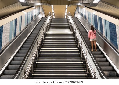 View Of Escalators With A Staircase In The Center In The Subway And A Woman On Her Back Going Up One Of The Escalators. Transport Concept