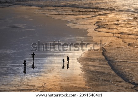 View of a family on wide sandy beach in the light of sunset - man photographing woman posing, boy and girl walking                         
