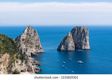 View of the Faraglioni from the Island of Capri. Holidaymakers with boats enjoy the scenery. 