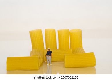 View of a fat man as a miniature figure. Behind him some pasta tubes. White background. Concept: lose weight reduce carbohydrates