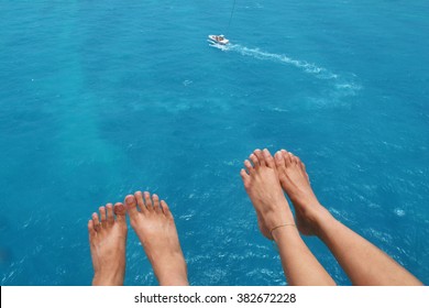 View of feet of couple parasailing with the speed boat in the sea background