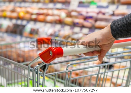 View of a female hand with pushcart in supermarket. The racks with the consumer goods in blur. Shallow depth of field