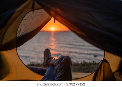 View of female legs in a tourist tent at sunset on the beach. The woman is hiking and camped on the riverbank.