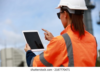 ฺBack View Female Site Engineer With Orange Safety Jacket And White Hard Hat Working On Digital Tablet At Construction Site Line, Engineering And Technology Concept  