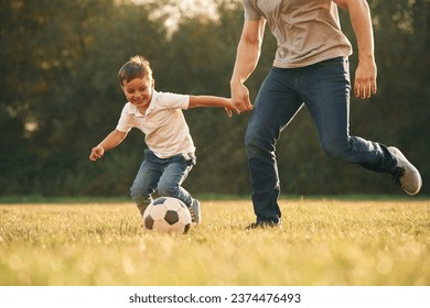 View of the field, with soccer ball. Father and little son are playing and having fun outdoors.