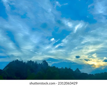 The view is filled with gentle morning light, accompanied by the warm radiance of the rising sun. The bright blue sky adorns the majestic natural scenery. Surrounding it, a beautiful green forest. - Shutterstock ID 2312063429