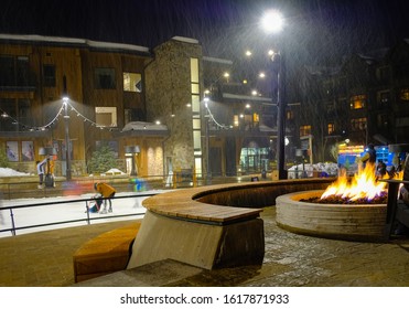 View Of Fire Pit With Burning Fire And Skating Rink Behind It In Aspen, Colorado, On Snowy Winter Night