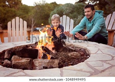 view of firepit and happy smiling family of two, father and son, warming their hands by the fire and enjoying time together in the background