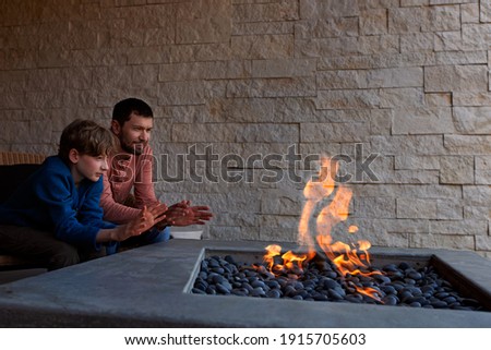 view of firepit and happy smiling family of two, father and son, warming their hands by the fire and enjoying time together 