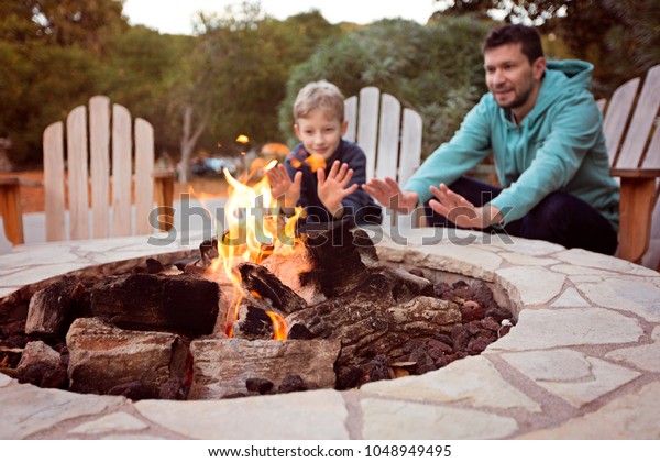 view of firepit and happy smiling family of\
two, father and son, warming their hands by the fire and enjoying\
time together in the\
background