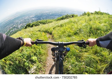 View From The First Person Of A Cyclist Riding Downhill From A High Mountain In The Background Of A City In The Distance