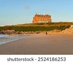 View of Fistral beach in Newquay, Cornwall, looking up to an iconic hotel building up on the headland. Sandy beach and blue sky.