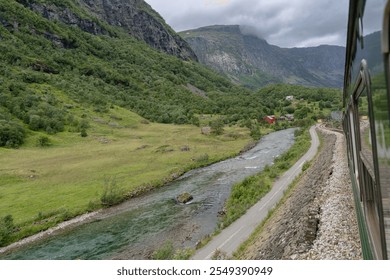 View of the Flam River winding through Flamsdalen Valley, surrounded by lush greenery, mountains, and cloudy skies, captured from the Flamsbana tourist train. Norwegian nature concept - Powered by Shutterstock