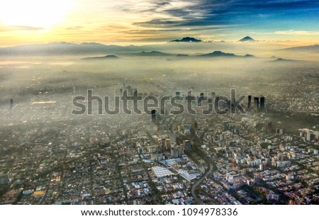 View flying over Mexico City in the morning with the buildings and mountains popping out of the fog and smog.