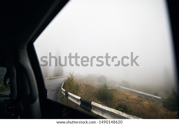 View of foggy mountain road with forest from the\
car window