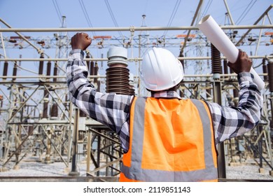View form back of handsome engineering man holding paper projects plan and wear hardhat for success in front of High power power plant. Back view of contractor on background of power plant buildings.