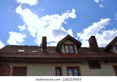 View of a fragment of a house with a roof in the background, a light blue sky with white clouds - Shutterstock ID 2282239055