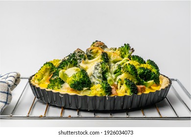 View of freshly baked homemade broccoli salmon quiche in metal oven pie baking plate on white background.