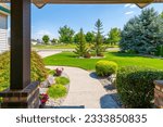 View from the front porch of a modern suburban home with a manicured front lawn in a nice community neighborhood across the street to a park on a sunny summer day.