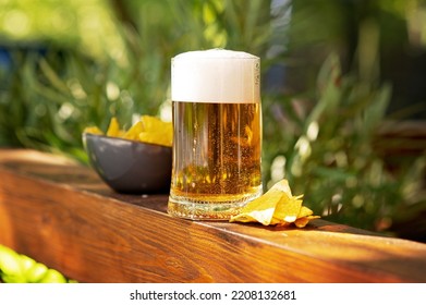 View of full beer glass from side with wooden deck background, outdoors and in daylight, lots of bubbles, beer has just been poured. Closeup of a glass of beer in the daylight - Shutterstock ID 2208132681
