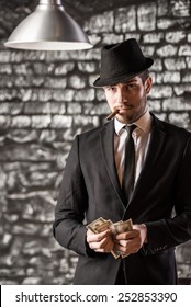 View of a gangster man is smoking a cuban cigar and holding money.