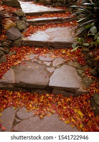 A view of garden stone steps covered by autumn leaves. The steps are made of wide stone tiles. Staircases can be used to symbolize achievements, a link of heavens and earth or spiritual enlightenment