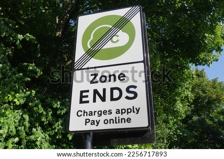 View of a generic clean air zone congestion charge road sign seen at the end of the zone with leafy green trees in the background