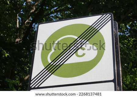 View of a generic clean air zone congestion charge road sign seen at the end of the zone with leafy green trees in the background