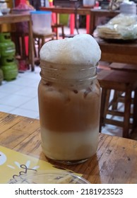 A View Of A Glass Of Iced Teh Tarik, Tea With Milk, Popular In Malay People, Placed On A Wooden Table With Background Blurred Food Stall Situation 