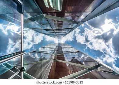 View up a glass skyscraper with the reflection of the dramatic sky in the glass on three sides