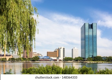A  view of a glass window skyscraper in downtown Toledo Ohio.   A beautiful  blue sky with white clouds reflecting in the glass windows. 