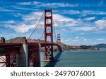 A view of the Golden Gate Bridge from The Presidio Park in San Francisco, California. It is a sunny day with a blue sky and clouds in the background.