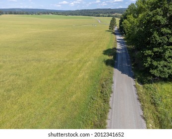 View Of Gravel Road, Large Green Agriculture Field And Trees. Aerial, Drone Photography Taken From Above In Sweden In Summer Time.