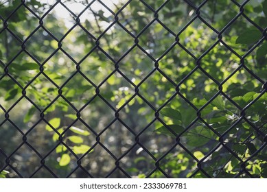 View of green leaves in a forest scene through a black chain link fence. Abstract geometric nature background. - Powered by Shutterstock