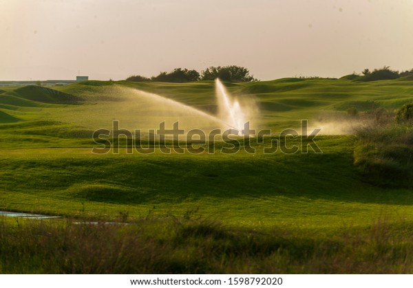 View of green rolling landscape and watering or\
sand traps on golf course
