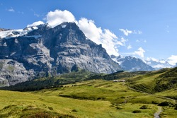 View To Grosse Scheidegg In The Grindelwald Valley, Swiss Alps, With Mountain Peak Visible In Clouds, And A Road Turn, Farms And Meadows In The Foreground