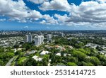 A view from Guaynabo, Puerto Rico, looking toward Metro San Juan in the distance. The scene features lush greenery, rolling hills, and cityscape buildings on the horizon under a blue skyline.