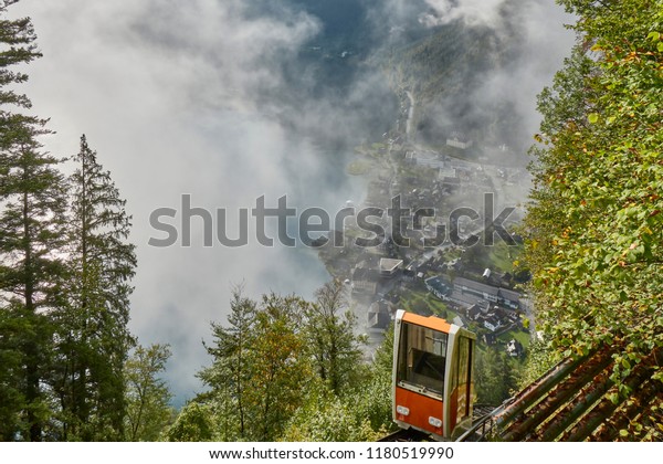 View of a\
Hallstatt cable car from the top station leading to a skywalk view\
in Austria with mist in the\
background.