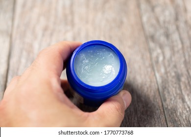 A View Of A Hand Holding A Container Of Topical Cough Suppressant Ointment.